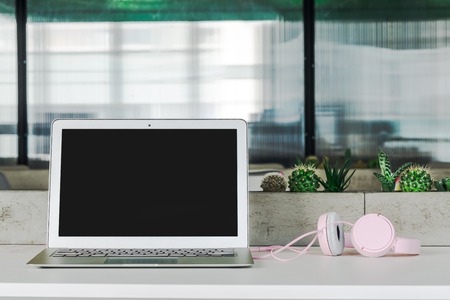 Work place in the modern office. A notebook with headphones is on a table with plantsの写真素材
