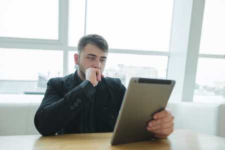 man sits in a modern cafe near the window and looks at his gadget. A businessman uses a tablet in a restaurant.の写真素材