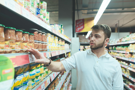 A handsome man makes a choice at the supermarket. A man buys canned food at the store. Shopping in a...