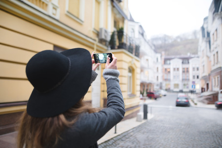 Stylish woman tourist makes a photograph of architecture. The girl is engaged in mobile photography. Street photos on the phone.の写真素材