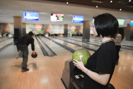 A girl with a ball for bowling in her hands looks at another person's game. Bowling gameの写真素材