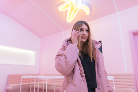 A beautiful girl speaks by phone in a room with a pink interiorの写真素材