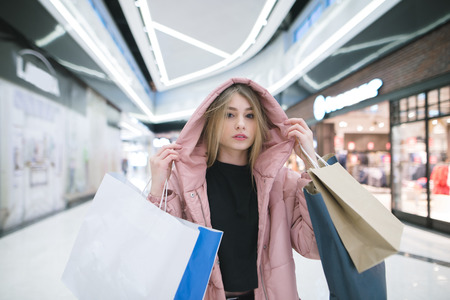 The life of a blonde in a pink smoker lays in the middle of a shopping center with purchases in his hands. Shopping.の写真素材