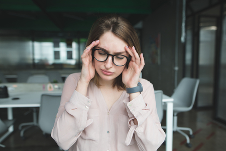 A female office worker has a headache. The girl raised her hands to her head through a headache. The main pain from work in the office.の写真素材