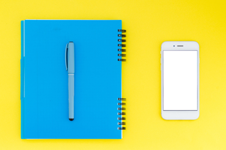 Blue notebook with a pen and a smartphone on a bright yellow background. Flat Lay Layoutの写真素材