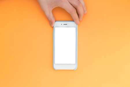 Flat lay hand with phone. The hand holds a smartphone with a white screen on top of a yellow background. Hand with phone isolated on yellow background.の写真素材