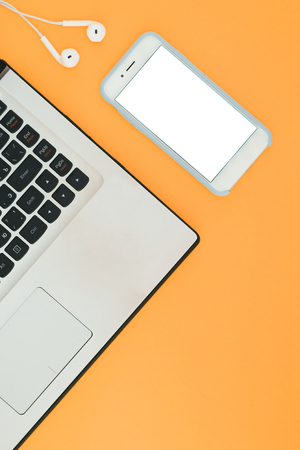 Laptop and smartphone with a white screen and headphones on the orange background. Minimalistic working space with a place for text. Flat Layの写真素材
