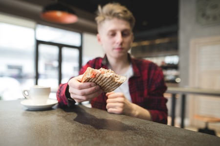 Panini sandwich close up. A young man offers a sandwich. Student with a sandwich sitting in a cafe. Focus on the sandwichの写真素材