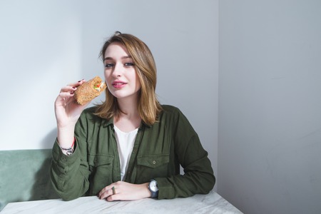 Portrait of a beautiful girl at the table and with a sandwich in her hands. A girl with a beturbist in her hands looks at the camera.の写真素材