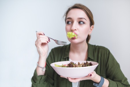 A funny woman eating salad greens. Costume with a plate of salad in his hands. Healthy eating and healthy foodの写真素材