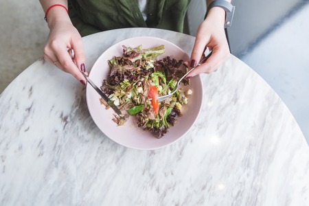 Hands of a woman and a plate of salad. A girl eating a salad in a light restaurant at the table...