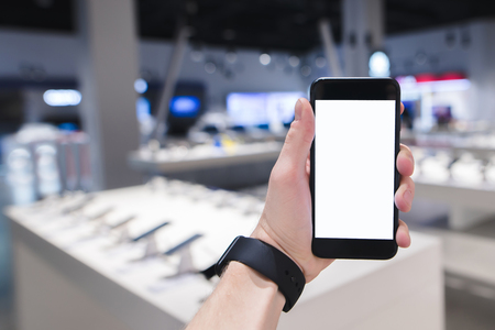 A person holds a smartphone in the background of a technology store. Phone against the background of a blurry store.の写真素材