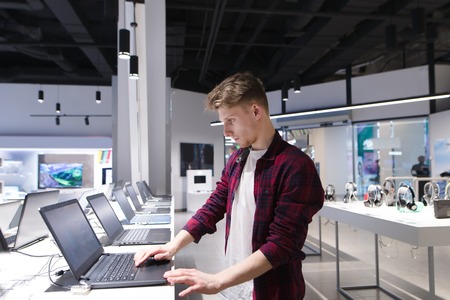 A young man chooses a laptop in an electronics store. A man looks at laptops in the computer department at the technology store. Buy a laptop.の写真素材
