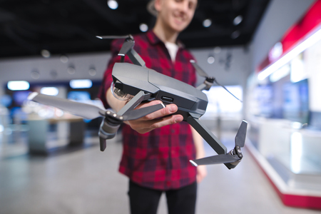 A positive young man with a quadcopter in his hands is in the drones store. Buy a dron at an...