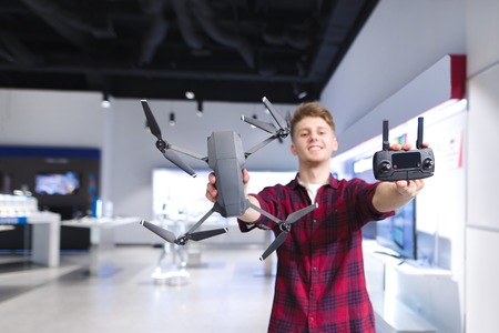 A positive young man holds a quadcopter in his hands and a control panel in the background of the...