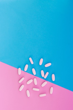 White pills lie on a colored background. Vitamins on blue and pink pastel background. Place for text. Top view.の写真素材
