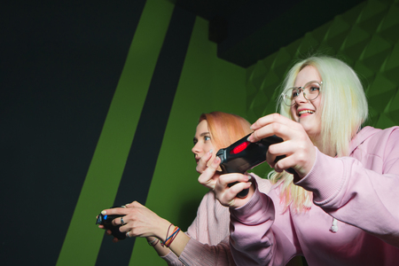 Gamepads in female hands close up. Emotional girlfriends with joysticks in their hands sit on the sofa on a green background and play video games.の写真素材