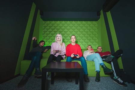 A group of friends sitting on the couch and playing games on the console. Many young people on the couch over the game on the game console.の写真素材