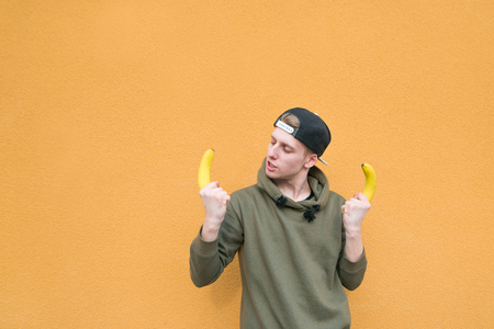 A funny young man standing on the background of an orange wall with bananas in his hands. A look at bananas.の写真素材