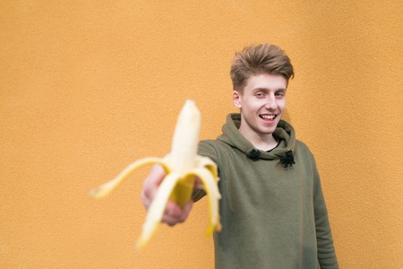 Positive young man standing on an orange background with a banana in his hand. Focus on the person.の写真素材