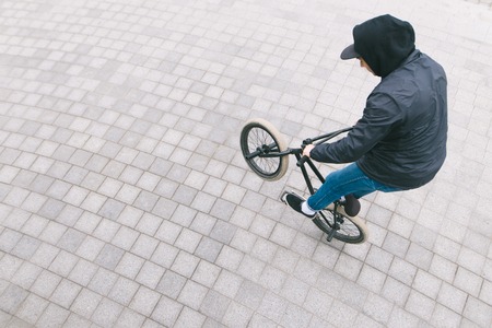 BMX freestyle. A young man in casual clothes makes tricks on a BMX bike. Top view.
