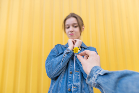 A man's hand gives a little flower to a girl on the background of a yellow wall. Flowers as a gift...