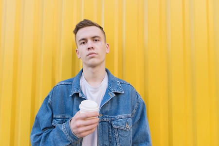 Portrait of a stylish young man with a cup of coffee in his hands on a yellow background. A young...