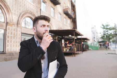 Busy man goes down the street, eats a sandwich and looks away. Business man is having a fast food trip to work.の写真素材