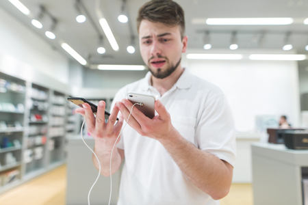 man chooses between two smartphones in a modern store. The buyer selects a smartphone in the...