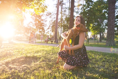 Cute girl hugs a beautiful young dog in a park on the background of a sunset. Embrace with the dog in the fresh air. Love is the owner and petの写真素材