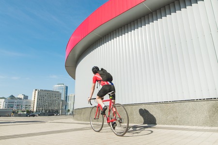 Back of a cyclist riding a red road bike against the backdrop of the city and modern architecture....
