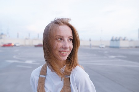 Outdoor portrait of a smiling red-haired girl with freckles on a city light background. Redheaded happy girl looks aside and smiles closeup portrait.の写真素材