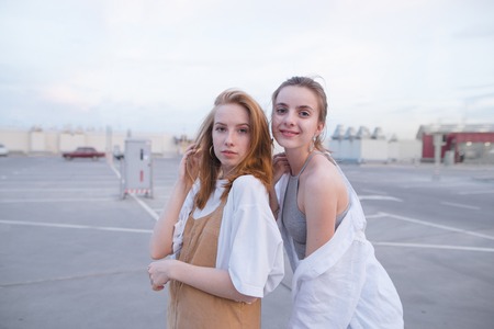 Two attractive girls are standing on the city background and looking at the camera. Street portrait...