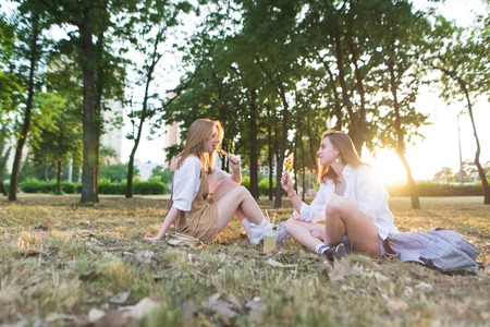 two young women sitting on grass hugging rear viewの写真素材