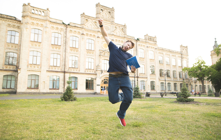 Happy student with books in his hands jumps on campus at the background of the university building. Emotional man with books in his hands jumping with joy. The student passed the examの写真素材