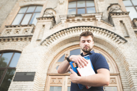 Portrait of a student with books in his hands against the background of a building of the old university. Man with a beard and a book in his hands stands on the background of the old architecture.の写真素材