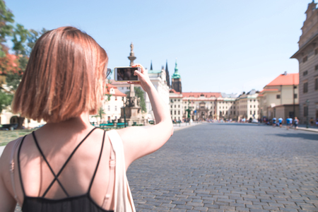 Tourist girl strolling through the old town and photographing the street on a smartphone. Tourist woman strolling through Prague, Czech Republicの写真素材