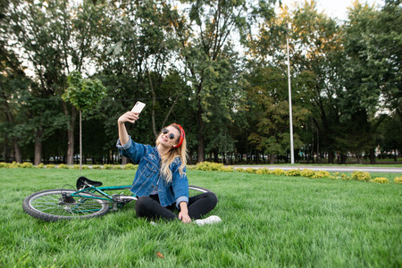 Young girl sits in the grass in park and takes selfie on a smartphone. Happy beautiful girl in...