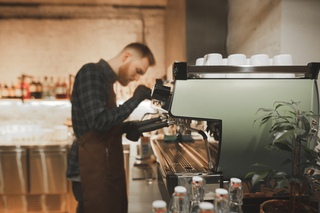 Bearded man barista steaming milk on a professional coffee machine. Process of cooking coffee on a coffee machine in the coffee shop. Focus on coffee machine. Background. Copyspaceの写真素材