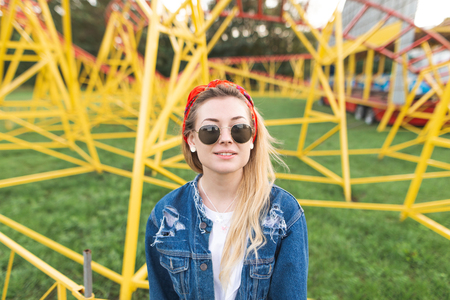 Portrait of an attractive girl in stylish clothes and sunglasses at the background of an amusement park, looking at the camera and smiling. Amusement Park conceptの写真素材
