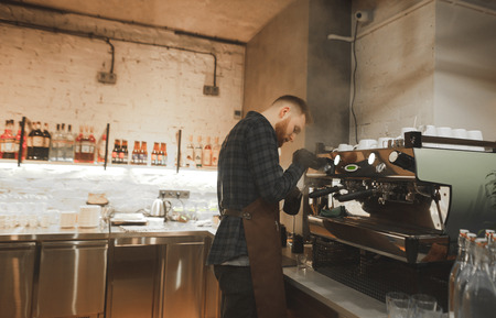 Barista's husband works on a professional coffee machine in a cozy cafe.Barista is a professional...