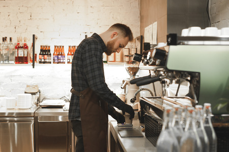 Bartender with a beard weighs coffee beans on the electronic scales at the coffee shop. Barista is...