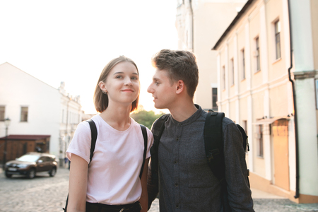 Portrait of a beautiful young couple against the street streets and sunset. Happy couple walking around the town in the evening. Man looks at the girl in love.の写真素材