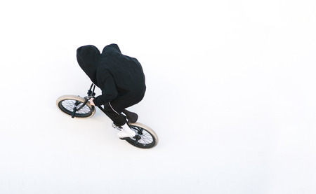 Portrait of a rider in dark clothes riding on a bmx on a white wall. bmx freestyle on a white...