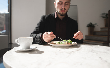 Cup of coffee in the background of a business man eating in a restaurant. Focus on the cup.