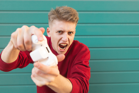 Emotional student gamer with a gamepad in his hands playing console games, looking into the camera...
