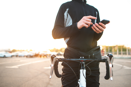 Close-up of a hand with a smartphone in a man with a bicycle. Bike rider rest and using a smartphone. Cyclist with a bike on the street in the sun and uses a smartphone. Copyspace.の写真素材