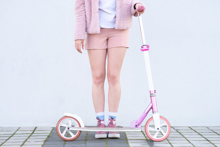 Pink scooter and girl in pink clothes on the background of a white wall. Legs and a kick scooter on...