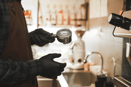 Barista holding portafilter making espresso coffee at the cafe at the coffee machine. Male bartender in the black gloves making cappuccino coffee at cafe. Close up photo.の写真素材