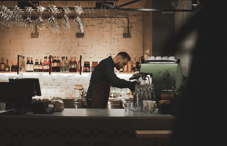 Barista at the restaurant bar counter.Portrait of a bartender with a job in a cozy restaurant.Owner of the restaurant prepares coffee in a professional coffee machine, stands behind a bar counterの写真素材